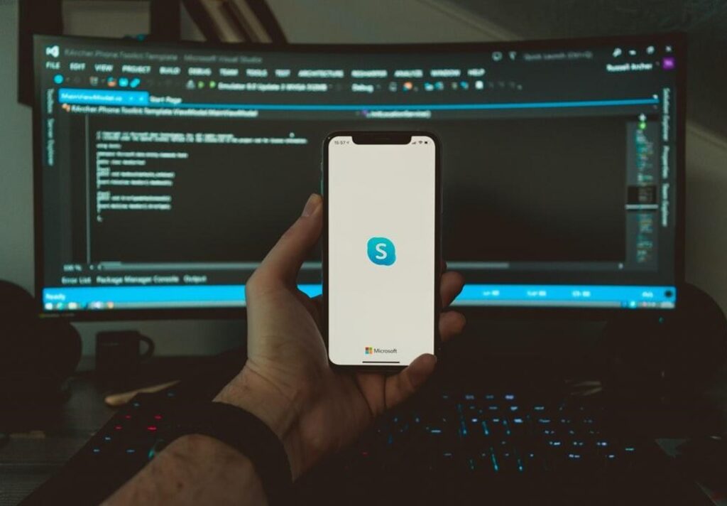 mans hand holding cell phone microsoft skype app large curved monitor