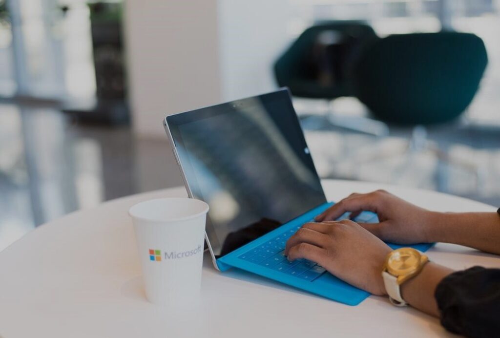 womens hands typing on Microsoft Surface Microsoft coffee cup