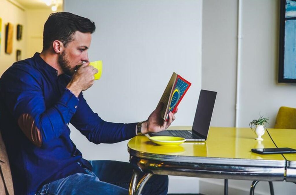 man drinking coffee with book and laptop