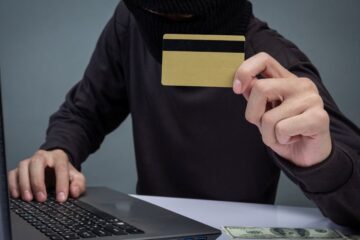 cybercrime - masked hacker with credit card in front of computer